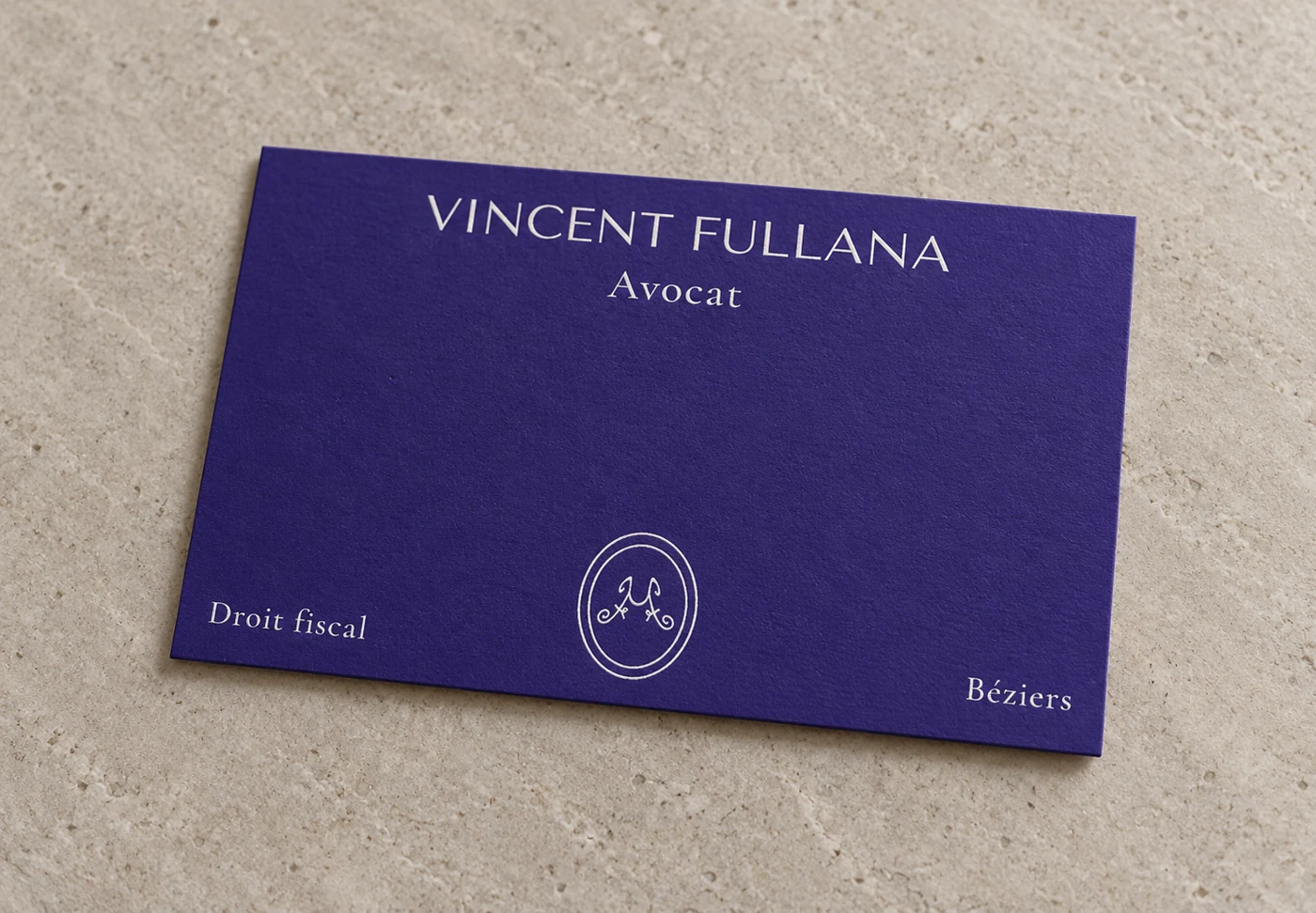 Carte de visite de Vincent Fullana, avocat, bleu outremer et lettres blanches, posée sur de la pierre